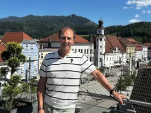 Ein Mann in heller Sommerkleidung steht auf einer Terrasse hoch über einer Stadt.