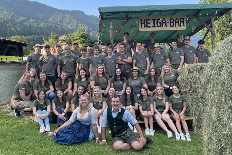 Eine Gruppe von Jugendlcihen posiert auf einer Wiese neben Heuballen vor einer planengedeckten Bar