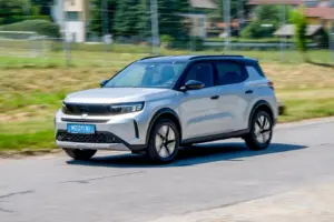 Ein silbergraues Fahrzeug der Kategorie Kompakt-SUV fährt auf einer Landstraße von rechts nach links