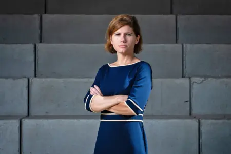 Ingrid Brodnig liest in Bruck Eine Frau im blauen Kleid steht mit verschränkten Armen vor einer Tribüne