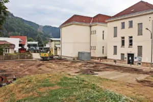 Bruck: Umbau des Schulhofs Berndorf läuft Ein Bagger arbeitet auf einer großen Erdfläche vor einem Haus