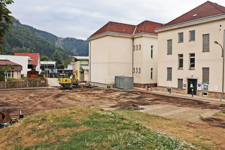 Ein Bagger arbeitet auf einer großen Erdfläche vor einem Haus