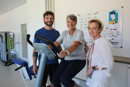Bruck: Ambulante Reha jetzt für alle Eine ältere Frau sitzt flankiert von zwei BetreuerInnen auf einem Ergometer