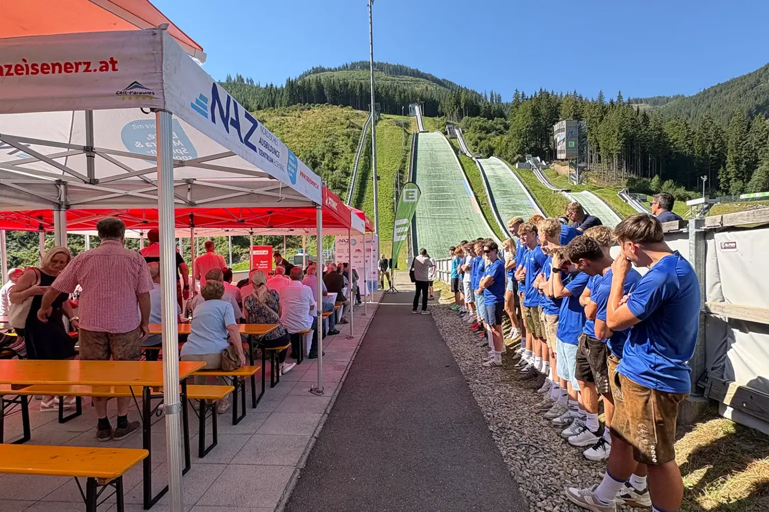 Schanzen-Geburtstag in Eisenerz Ein Festgelände im Freien mit Zelten, Pavillons und Menschen, im Hintergrund Schisprungschanzen
