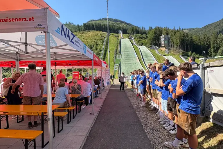 Schanzen-Geburtstag in Eisenerz Ein Festgelände im Freien mit Zelten, Pavillons und Menschen, im Hintergrund Schisprungschanzen