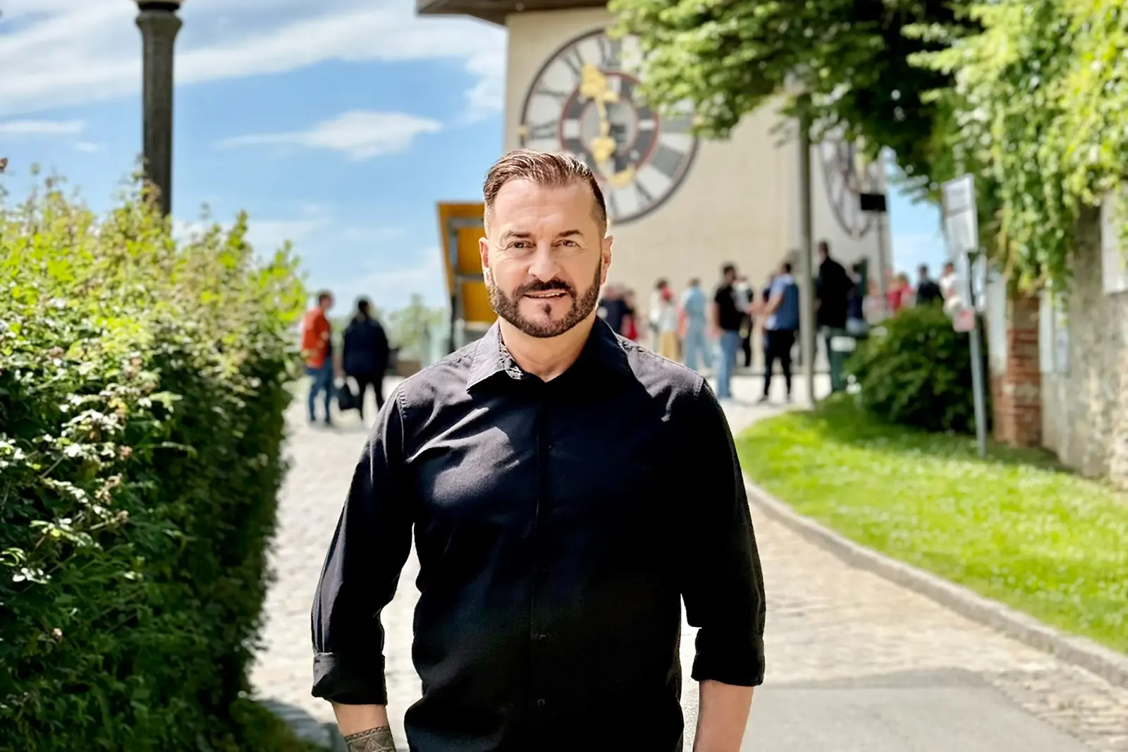 Ein Mann mit Bart steht vor einem Uhrturm