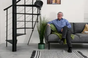 Ein Mann sitzt bequem auf einer Couch, daneben eine Wendeltreppe aus Metall.