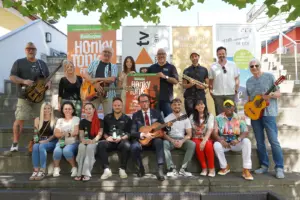 Eine große Gruppe von Personen posiert mit Musikinstrumenten und einem Plakat auf einer Treppe im Freien