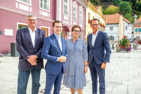 Eine Frau in gestreiftem Kleid und drei Männer in Anzügen stehen auf einem innerstädtischen Platz