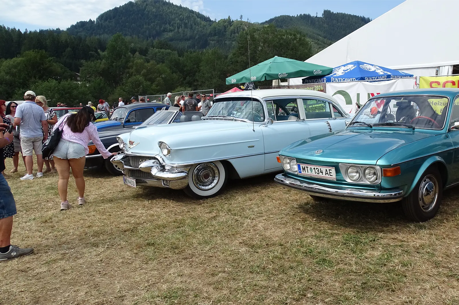 Oldtimer-Fahrzeuge stehen auf einer Wiese, dazwischen Menschen, im Hintergrund ein Festzelt