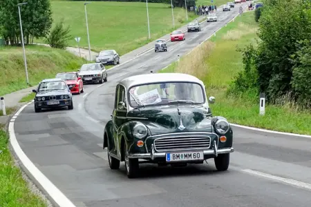 Oldtimertreffen in Parschlug – Fotogalerie Ein Oldtimerfahrzeug auf einer Landstraße, gefolgt von weiteren Autos älteren Baujahrs