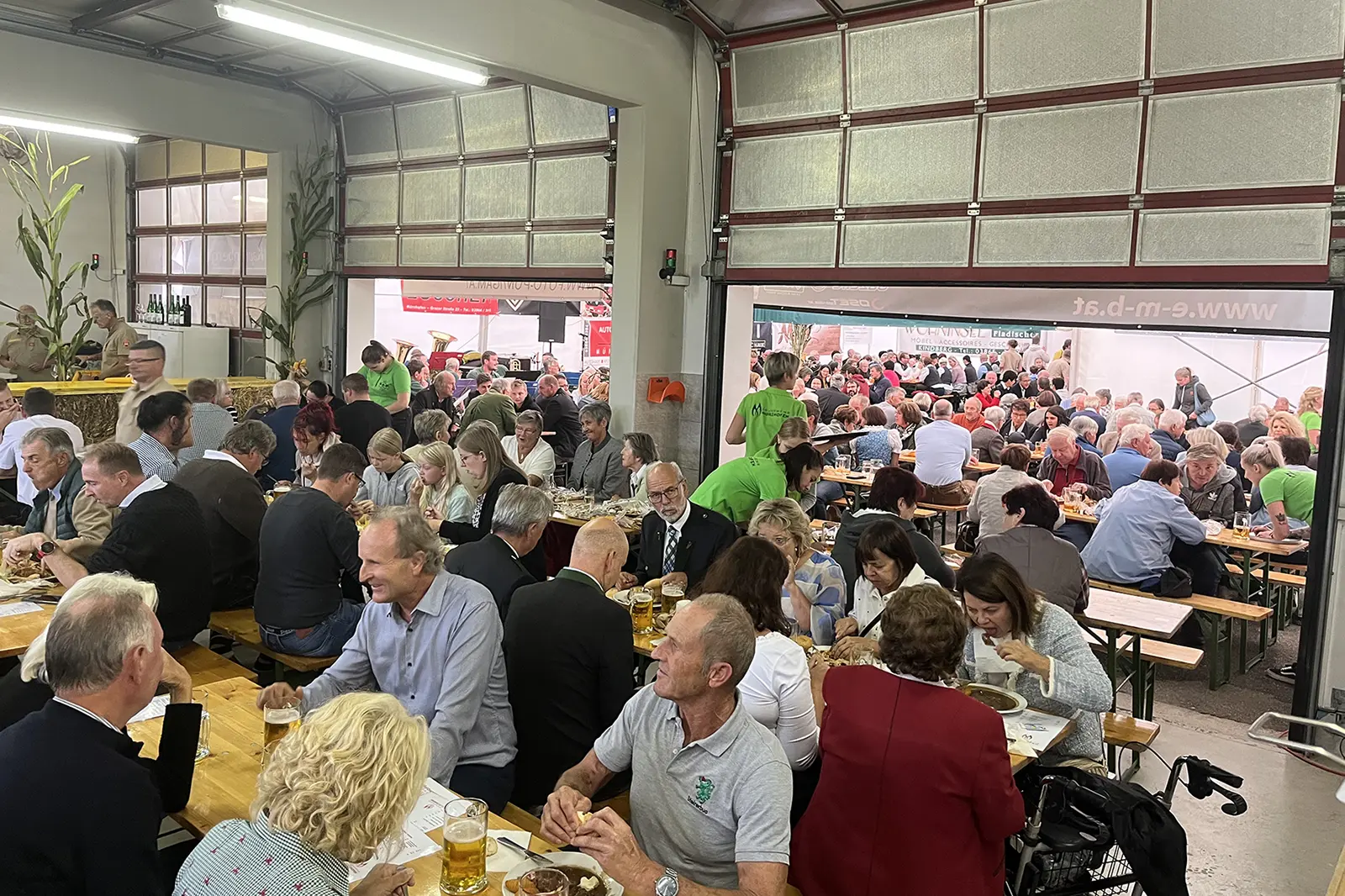 Viele Personen sitzen an Biertischen in einer großen Garage