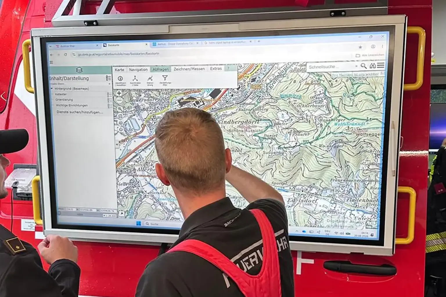 Ein Mann in Feuerwehrkleidung steht vor einem großen Bildschirm