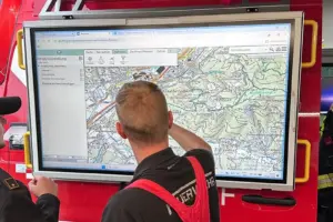 Ein Mann in Feuerwehrkleidung steht vor einem großen Bildschirm