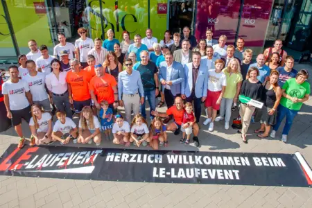 Beim LE-Laufevent schlägt die gute Stunde Eine Gruppe von mehr als 50 Personen, vor ihnen ein auf dem Boden ausgerolltes Transparent mit der Aufschrift "Herzlich willkommen beim LE-Laufevent"