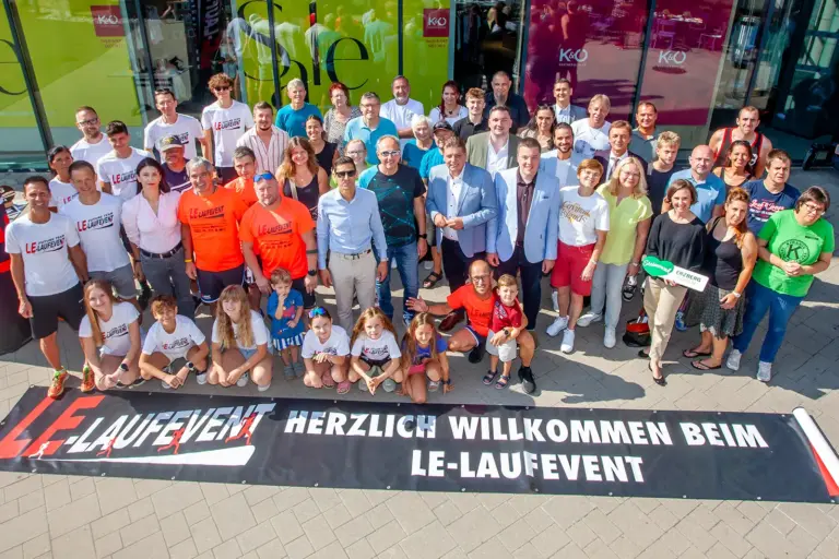 Beim LE-Laufevent schlägt die gute Stunde Eine Gruppe von mehr als 50 Personen, vor ihnen ein auf dem Boden ausgerolltes Transparent mit der Aufschrift "Herzlich willkommen beim LE-Laufevent"