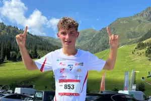 Ein junger Mann in Sportkleidung mit erhobenen Armen vor Gebirgskulisse