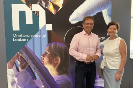 Leoben: Musik trifft auf Wissenschaft Ein Mann und eine Frau stehen vor einer Wand mit dem Logo der Montanuniversität Leoben