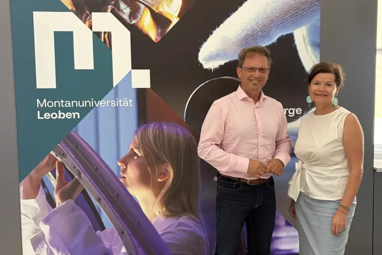 Leoben: Musik trifft auf Wissenschaft Ein Mann und eine Frau stehen vor einer Wand mit dem Logo der Montanuniversität Leoben