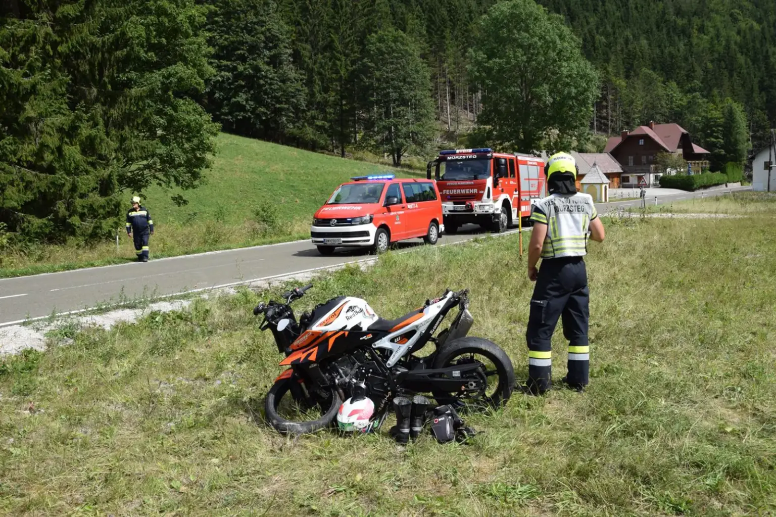 Motorradunfall in Mürzsteg Ein beschädigtes Motorrad in einer Wiese, daneben ein Feuerwehrmann, im Hintergrund zwei Feuerwehrfahrzeuge auf einer Straße