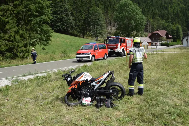 Motorradunfall in Mürzsteg Ein beschädigtes Motorrad in einer Wiese, daneben ein Feuerwehrmann, im Hintergrund zwei Feuerwehrfahrzeuge auf einer Straße
