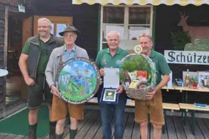 Vier Männer in jagdlicher Kleidung mit einer Zielscheibe, einer Plakette und einem Geschenkkorb in Händen