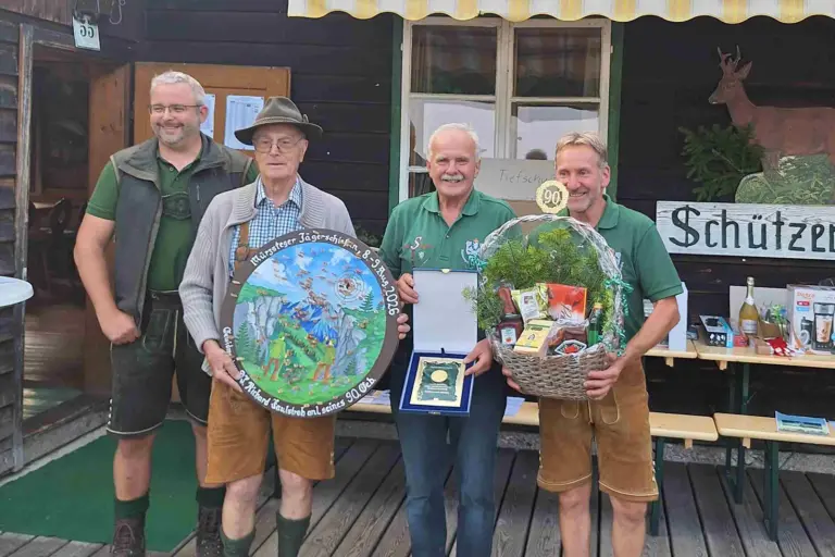 Vier Männer in jagdlicher Kleidung mit einer Zielscheibe, einer Plakette und einem Geschenkkorb in Händen