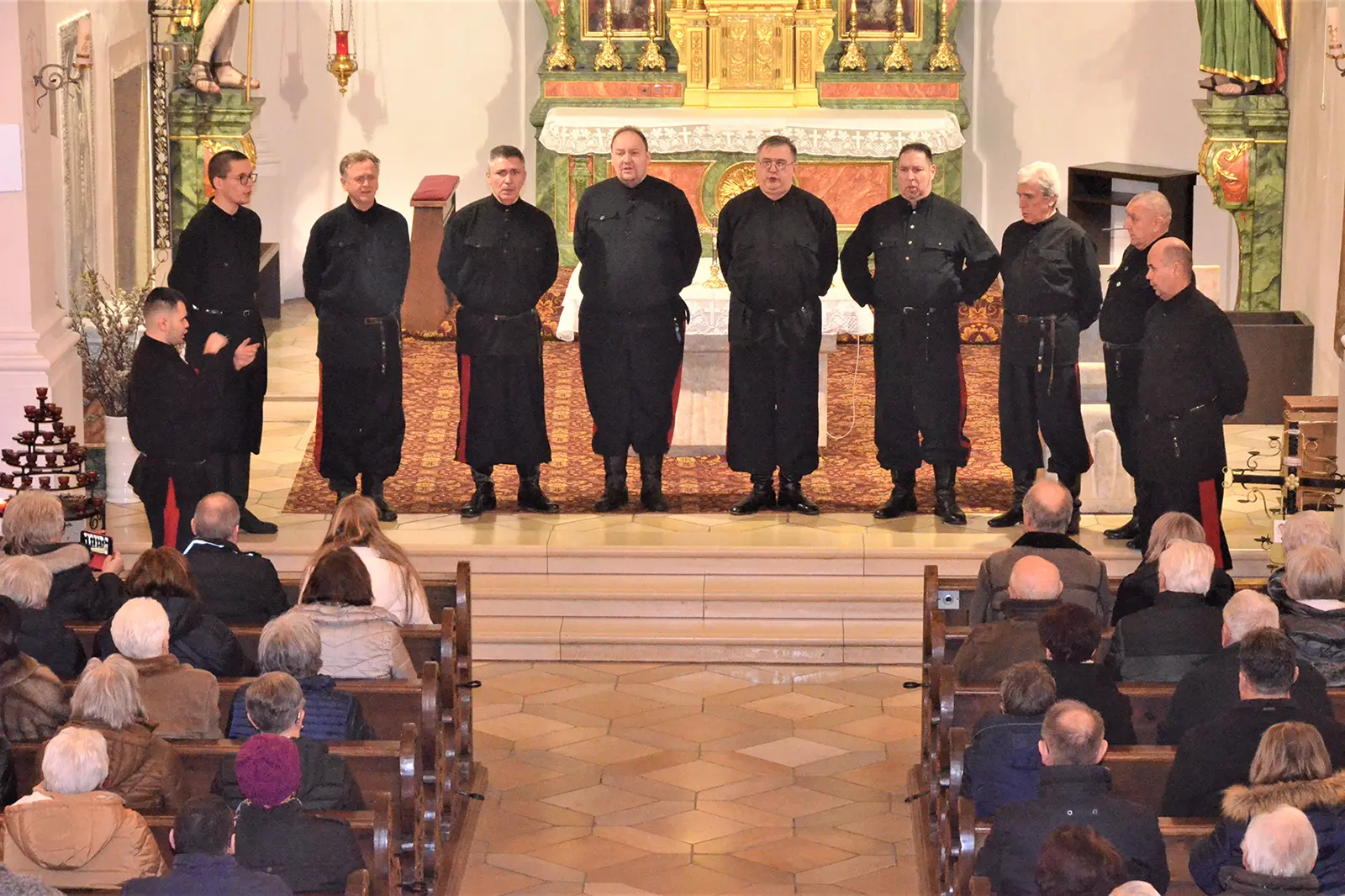 Eine Gruppe von Männern in schwarzer Kleidung steht vor Publikum in einer Kirche