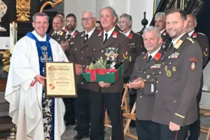 Mehrere Männer in Uniform stehen mit einem Geistlichen mit einer Urkunden in einer Kirche