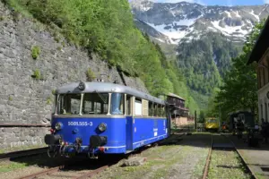 Ein blaues Schienenfahrzeug für den Personentransport auf Gleisen vor einer Gebirgskulisse