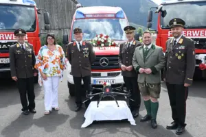 Eine Frau und fünf Männer, vier davon in Feuerwehruniform, mit drei Feuerwehrfahrzeugen und einer Drohne