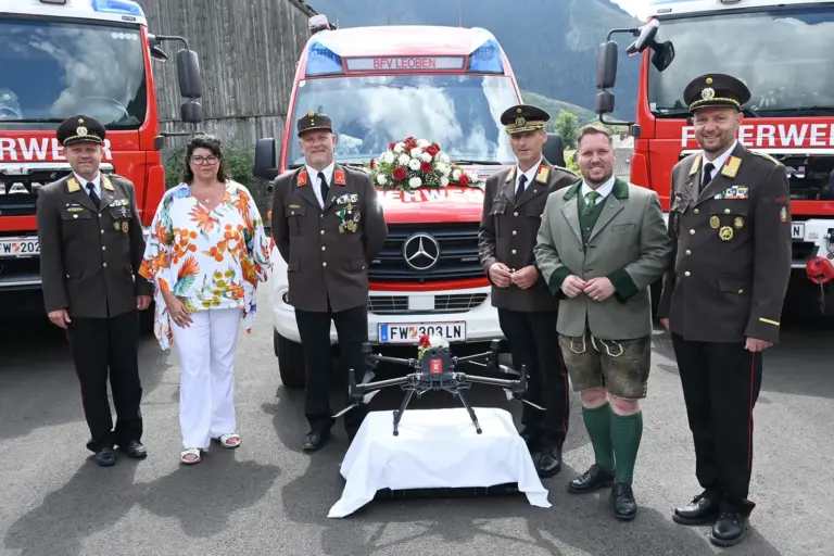 Neues Rüsthaus in Vordernberg eröffnet Eine Frau und fünf Männer, vier davon in Feuerwehruniform, mit drei Feuerwehrfahrzeugen und einer Drohne