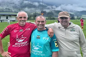 Drei Männer stehen nebeneinander auf einem Fußballplatz.