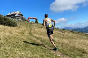 Gedenklauf zum Aflenzer Schönleitenhaus Ein Läufer läuft auf einem schmalen Bergweg über eine Almwiese bergauf. Vor ihm befinden sich eine Berghütte und weitere Teilnehmer, im Hintergrund ist eine Berglandschaft zu sehen.
