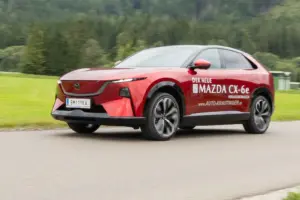 Ein rotes Fahrzeug der Karosserieform SUV fährt auf einer Landstraße von rechts nach links