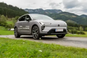 Ein grauer Pkw fährt auf einer Landstraße von links nach rechts, im Hintergrund eine Berglandschaft
