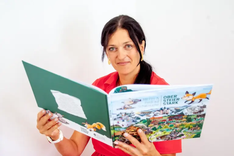 Booktober – ein Monat ganz im Zeichen der Bücher Eine Frau mit einem aufgeschlagenen Bilderbuch in Händen.