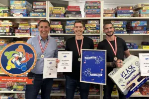 Meisterschaft der Spielefreunde in Bruck Drei Männer stehen mit Urkunden und Preisen vor einem Regal mit Spielen