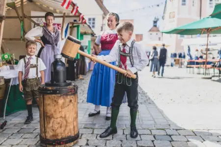 Botschafter der Volkskultur aus Bruck Zwei Buben in Tracht spielen vor zwei Fauen im Dirndl mit einem großen Hammer
