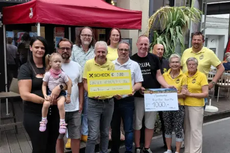 Eine Gruppe von Erwachsenen und einem Kind posiert bei einer Spendenübergabe vor einem Lokal. Im Mittelpunkt werden zwei Spendenschecks über 9.000 Euro und 1.000 Euro präsentiert.