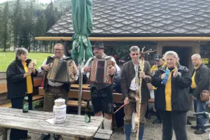 Eine Gruppe von Musikanten in Tracht spielt vor einer Hütte im Grünen