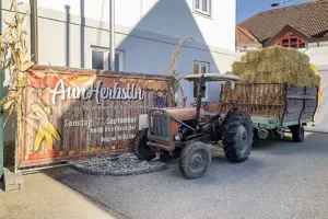 Ein Oldtimer-Traktor mit Ladewagen voller Strohballen steht neben einer Plakatwand