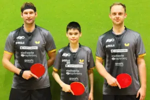 Drei Tischtennisspieler in einheitlichen grauen Trikots stehen mit ihren Schlägern vor einer grünen Wand.
