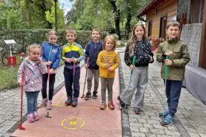 Sieben Kinder stehen mit Golfschlägern auf einer Minigolfbahn