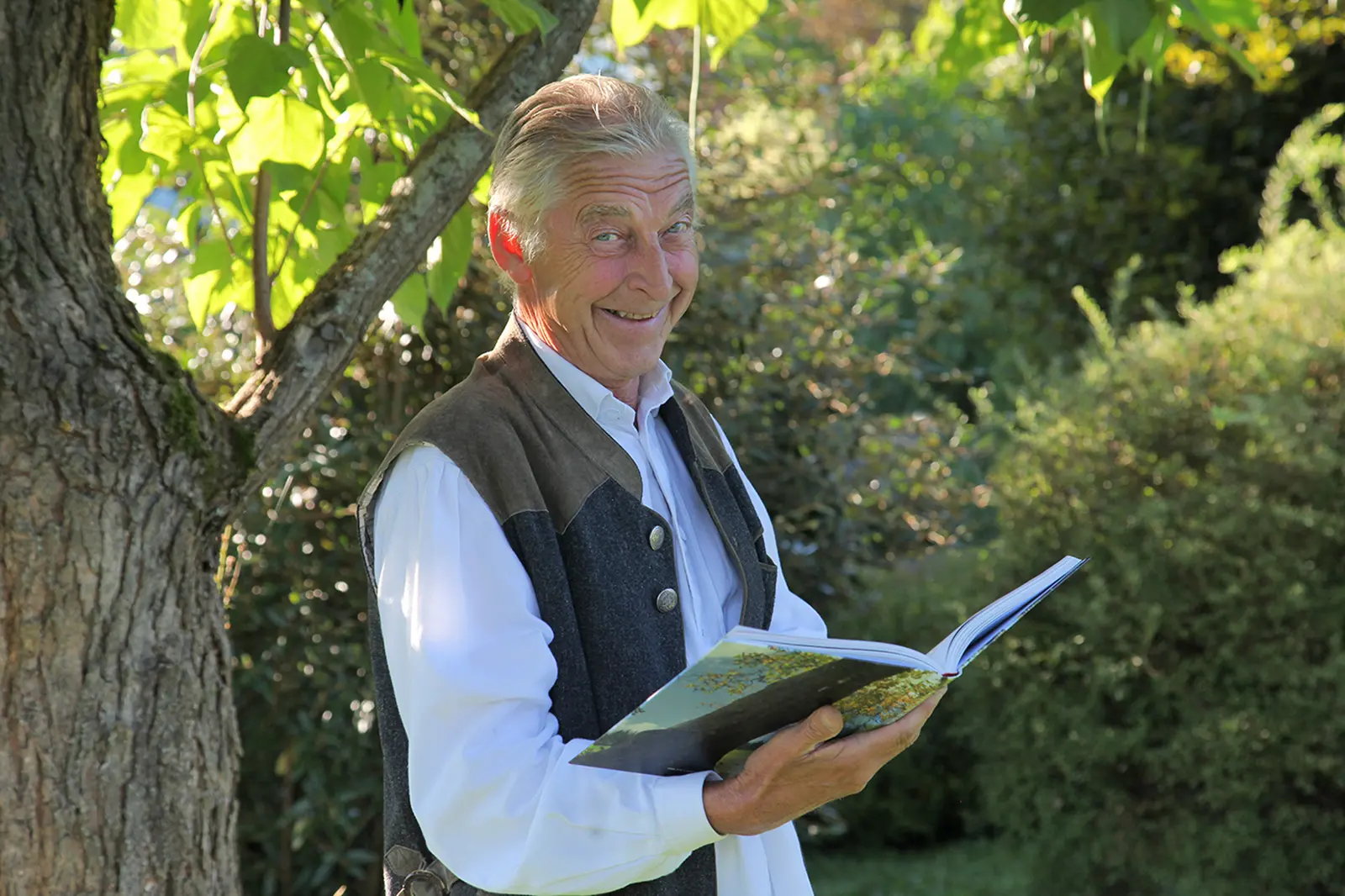 Ein älterer Mann steht mit einem Buch neben einem Baum