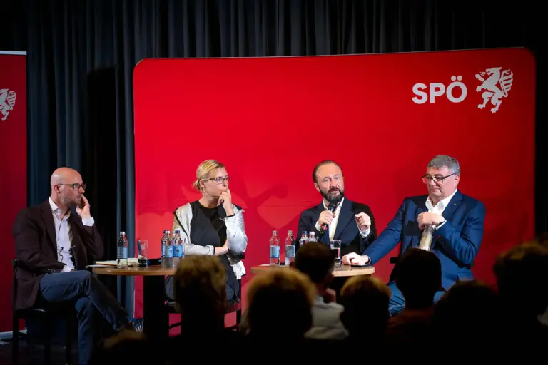 Leoben: Diskussion über Extremismus Drei Männer und eine Frau sitzen an einem Tisch auf einer Bühhe vor rotem Hintergrund