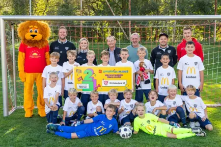 Neue Dressen für Hinterberger Nachwuchskicker Eine Nachwuchsfußballmannschaft des SV Hinterberg posiert mit Trainern, Betreuern und einem Löwenmaskottchen vor einem Fußballtor. Die Kinder präsentieren eine Urkunde für den zweiten Platz.
