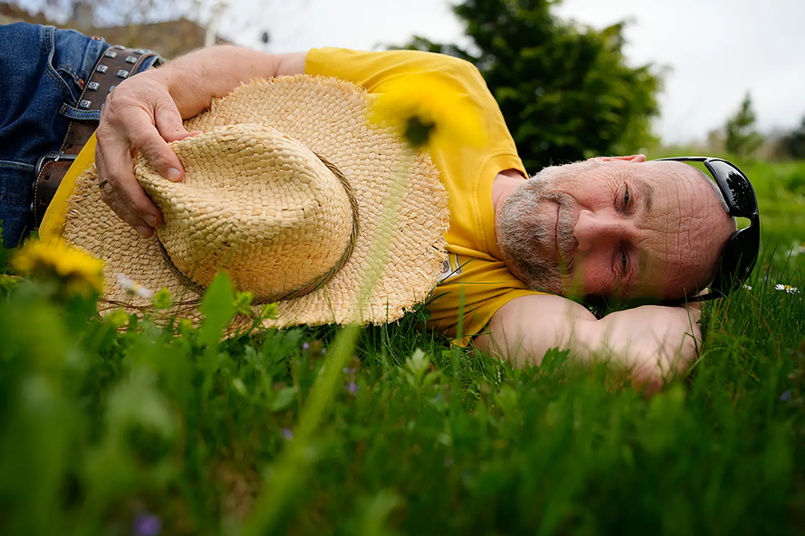 Ein Mann mit Sonnenbrille und Strohhut liegt im Gras