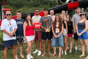 Eine Gruppe von Personen in leichter Beklediung steht mit einem Pokal auf einer Wiese