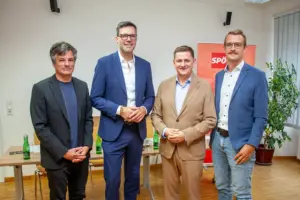 Vier Männer in Sakkos stehen lächelnd nebeneinander